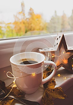 Cup of coffee, autumn leaves and Christmas lights on a window with a view
