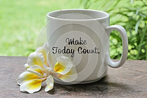 A cup of coffee with Bali frangipani flower on the wooden table with inspirational motivational quote on it - Make today count.