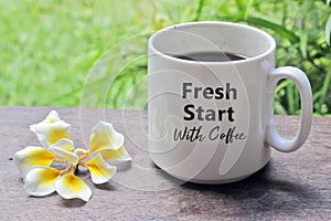 A cup of coffee with Bali frangipani flower on the wooden table with inspirational quote on it - Fresh start with coffee.
