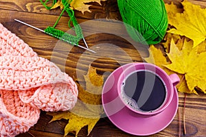 Cup of coffee, ball of yarn, knitting, knitted scarf and yellow maple leaves on a wooden table. Autumn still life