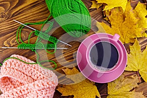 Cup of coffee, ball of yarn, knitting, knitted scarf and yellow maple leaves on wooden table. Autumn still life