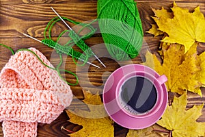 Cup of coffee, ball of yarn, knitting, knitted scarf and yellow maple leaves on wooden table. Autumn still life