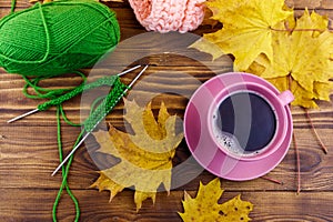 Cup of coffee, ball of yarn, knitting, knitted scarf and yellow maple leaves on wooden table. Autumn still life