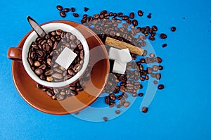 Cup of coffee with beans from above on blue background with cinnamon and sugar
