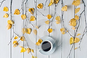 cup of coffee in the in birch branches with yellow leaves  on white retro wood boards. background. Autumn, fall concept. Flat lay