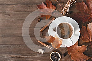 Cup of coffee with black coffee in a saucer on a wooden background, cinnamon,   red fallen autumn leaves, flat lay