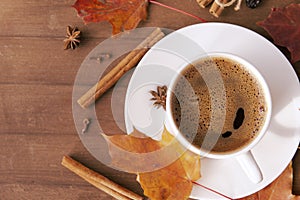 Cup of coffee with black coffee in a saucer on a wooden background, red fallen autumn leaves, cinnamon,  flat lay