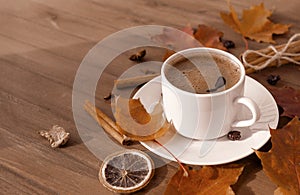 Cup of coffee with black coffee in a saucer on a wooden background, red fallen autumn leaves, cinnamon, a slice of dried orange