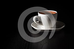 Cup of coffee on black wood table. White porcelain cup on saucer. Copy space