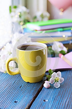 Cup of coffee, blank notebook, apple tree flowers and a stack of books, on a wooden windowsill