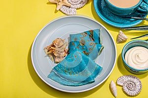 A cup of coffee and blue thin pancakes in a marine style. Starfish, sea shells, palm leaves