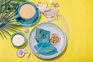 A cup of coffee and blue thin pancakes in a marine style. Starfish, sea shells, palm leaves