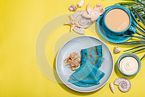 A cup of coffee and blue thin pancakes in a marine style. Starfish, sea shells, palm leaves