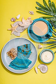 A cup of coffee and blue thin pancakes in a marine style. Starfish, sea shells, palm leaves