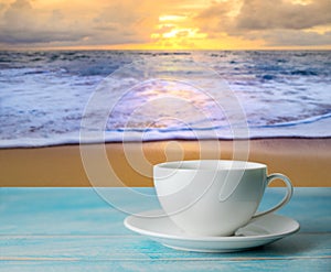 A cup of coffee with blurred beach sunset or sunrise and colorful of cloud sky in twilight