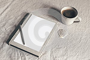 Cup of coffee, book, blank sheet of paper and silver pen. Moody breakfast table stationery mockup scene. Beige linen