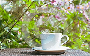A cup of coffee and book on the wooden table with morning light and blurred nature background