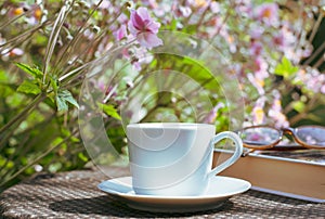 A cup of coffee and book on the wooden table with morning light and blurred nature background