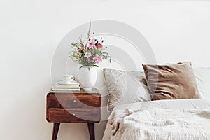 Cup of coffee and books on retro wooden bedside table. Rustic white ceramic vase with bouquet of pink cocmos and zinnia