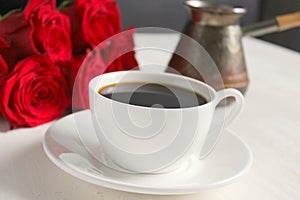 A Cup of coffee and a bouquet of red roses on the table close-up.
