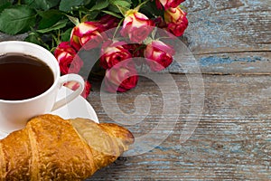 Cup of coffee with bouquet of roses and croissant on a wooden b