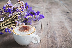 A cup of coffee with bouquet of violet dried flowers on wooden f