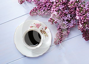 Cup of coffee and branches of blooming lilac on wooden table