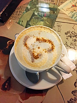 A Cup of coffee cappuccino with a heart of cinnamon on the table in the cafe