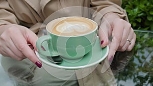 Cup of coffee cappuccino or latte in woman hands outdoors in coffee house or cafe. Classic heart shaped latte art on