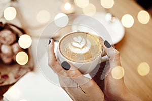 Cup of coffee cappuccino in woman hands, view from above, bokeh, rose flowers in cafe