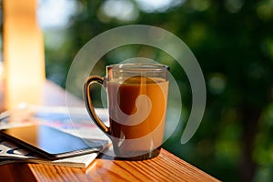 Cup of coffee and cellphone on the windowsill over blurred forest background at sunny summer day.