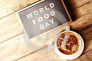 The cup of coffee and chalkboard with World Food Day text on wooden background