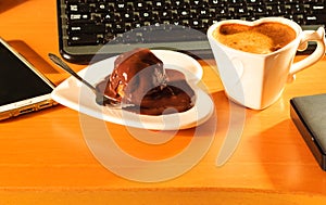 Cup of coffee and chocolate cake next to computer.