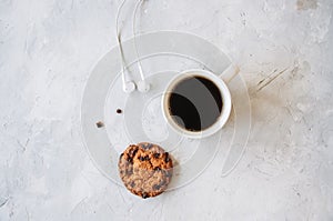 A cup of coffee chocolate chip cookie and headphones on a white