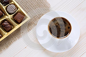 Cup of coffee and chocolates of allsorts on a wooden background