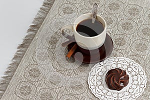 Cup of coffee with cinnamon and chocolate marsh-mallow on mat against monochromic tablecloth with copy space