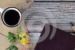 Cup of coffee and closed holy bible book on wooden background with spring flower and vintage paper, top view