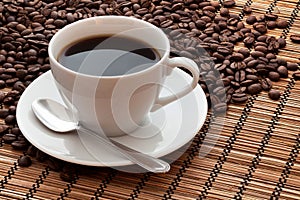 Una tazza di caffè e chicchi di caffè su una stuoia di bambù.