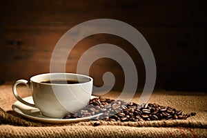 Cup of coffee and coffee beans on burlap sack on old wooden background