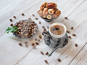 Cup of coffee, coffee beans and fresh dates on white wooden background