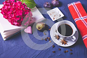 A cup of coffee, coffee beans and sugar cubes, an open book and a branch of hydrangea