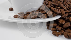 A cup of coffee and coffee beans on a white background. Roasted coffee beans on a white saucer, close up