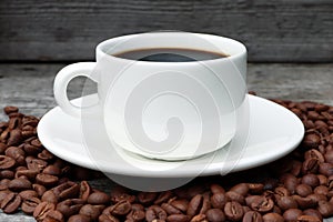 A cup of coffee and coffee beans on a wooden background. White coffee cup and saucer. Espresso.Roasted coffee beans