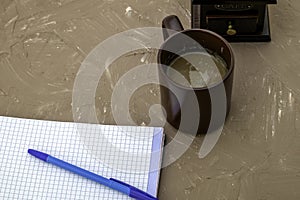 a cup of coffee a coffee grinder and a notebook with a fountain pen on the beige surface of copyspace