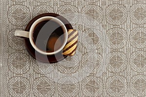 Cup of coffee and cookie on plate against monochromic tablecloth with copy space