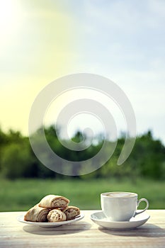Cup of coffee and cookie on wooden table in the summer garden.