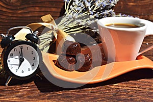 Cup of coffee and cookies with alarm clock and lavender on wood background