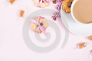 Cup of coffee with cookies, candies and lilac flowers on pink ba