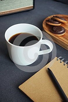 Cup of coffee with cookies next to notepad and music column