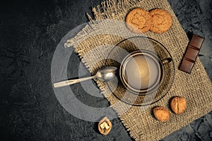 Cup of coffee with cookies, walnuts and chocolate on a burlap napkin on a dark concrete background. Creative mockup with free